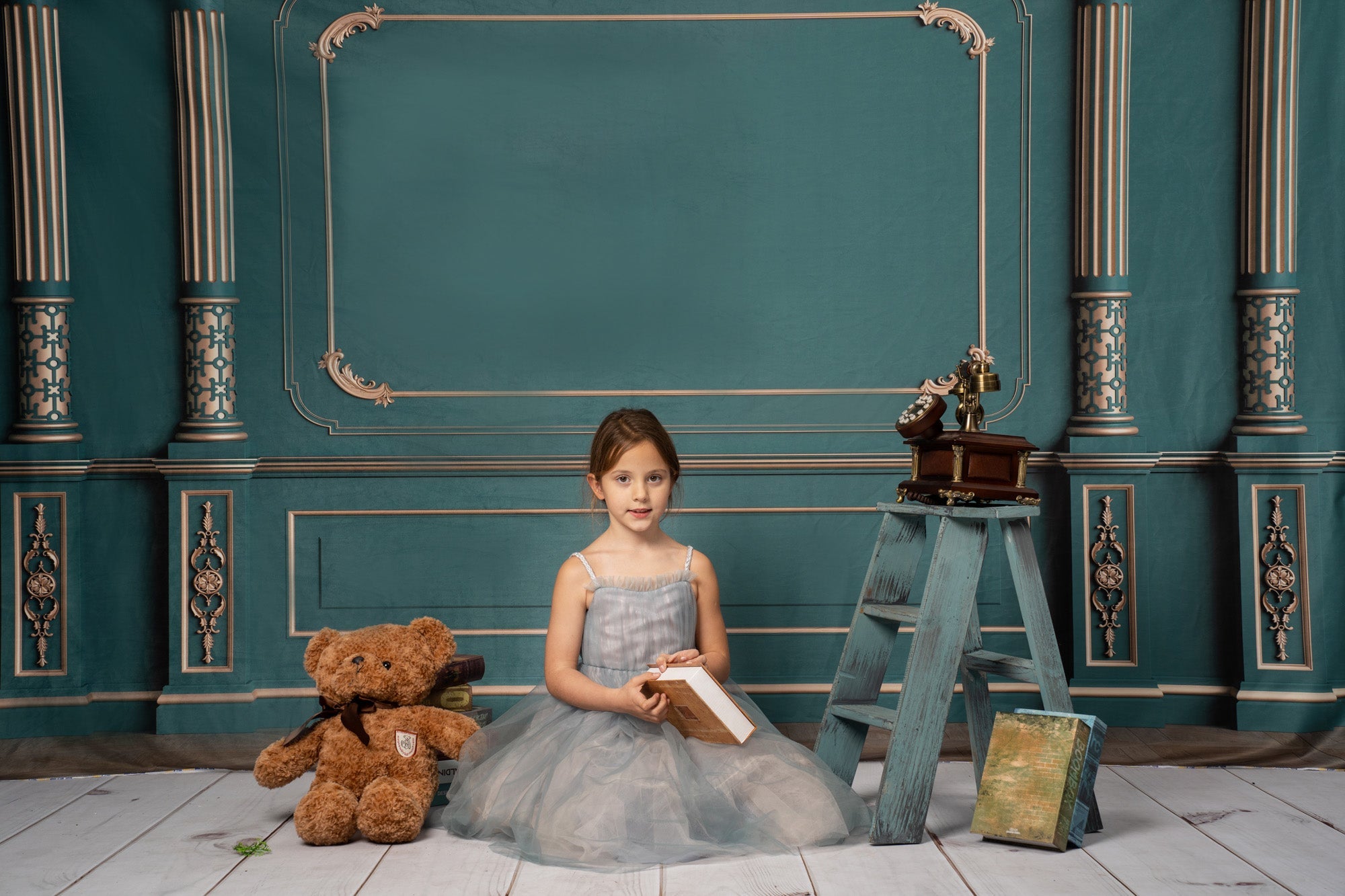 Ein Mädchen liest ein Buch vor einer grünen Wand, neben einem Teddybären