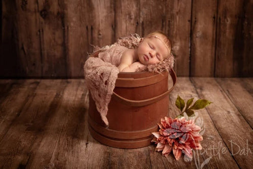 Ein Baby liegt in einem Holzeimer mit dahinterliegenden Holzwandpaneelen